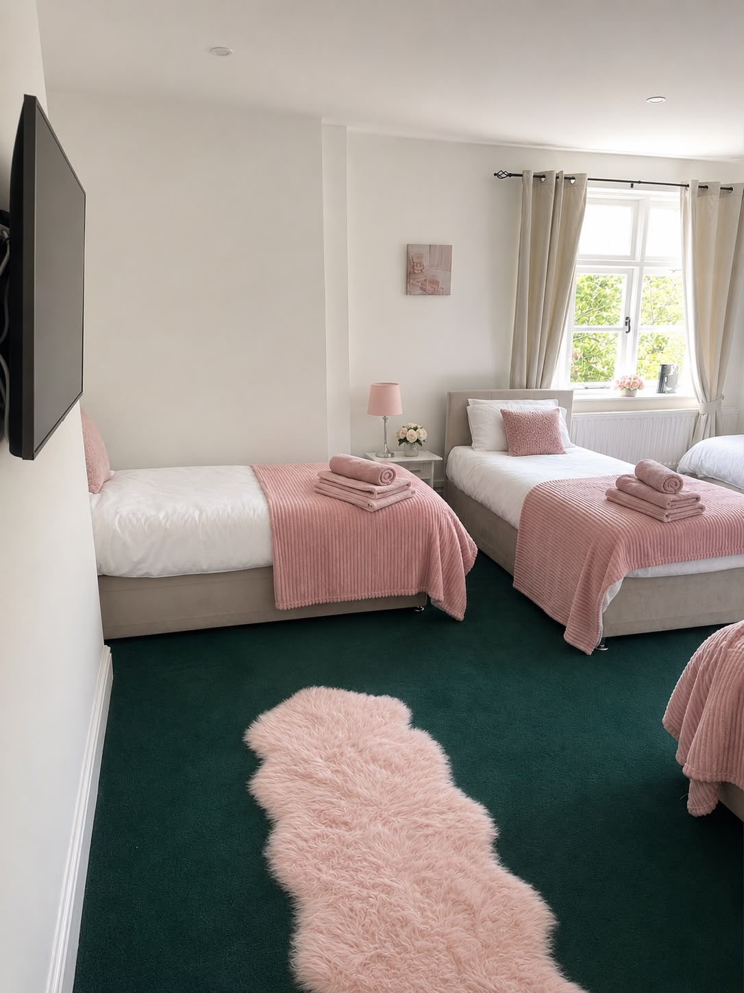 Two more of the beds in the shared room, made up with pink throws and rolled towels on dark green carpet